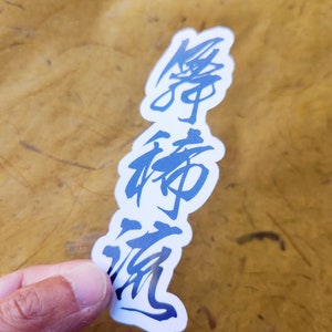 Puede incluir: Una pegatina blanca con caligraf&iacute;a negra que dice "夢 諦 勿" en japon&eacute;s.