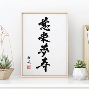 May include: A framed wall art print featuring vertical black ink calligraphy characters on a white background. The artwork includes a small black signature and a square red seal stamp in the lower left corner, encased in a light wood frame.