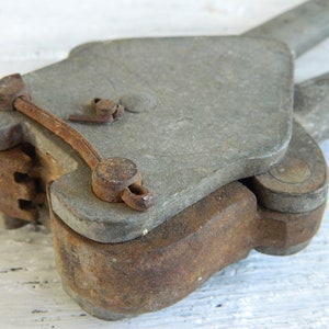 May include: A vintage metal tool with a rusty finish. The tool has a lever and a hinged jaw. It is likely used for crimping or fastening.