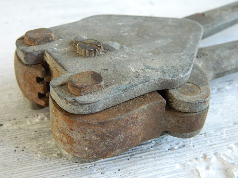 K&ouml;nnte beinhalten: Nahaufnahme eines rostigen Metallwerkzeugs mit Griff und Hebel. Das Werkzeug hat eine abgenutzte, graue Oberfl&auml;che und einen kleinen, runden Knopf oben.