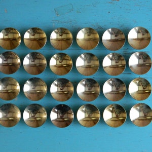 May include: A set of 20 gold-colored metal decorative round dishes arranged in a grid pattern on a blue surface.