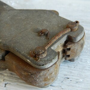 K&ouml;nnte beinhalten: Nahaufnahme eines antiken, rostigen Metallwerkzeugs mit einem Scharnier und einem Hebel. Das Werkzeug hat eine abgenutzte, graue Oberfl&auml;che und zeigt Spuren von Alter und Gebrauch.