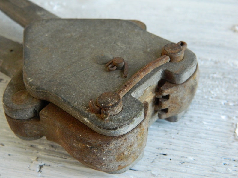 K&ouml;nnte beinhalten: Nahaufnahme eines antiken, rostigen Metallwerkzeugs mit einem Scharnier und einem Hebel. Das Werkzeug hat eine abgenutzte, graue Oberfl&auml;che und zeigt Spuren von Alter und Gebrauch.