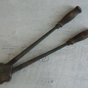 K&ouml;nnte beinhalten: Ein Vintage-Werkzeug aus Metall mit zwei Holzgriffen. Das Werkzeug hat einen Metallkopf mit einem Hebel und eine Metallplatte mit einem Loch in der Mitte. Das Werkzeug wird zum Verpressen von Metall verwendet.