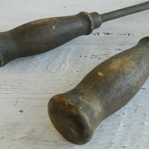 K&ouml;nnte beinhalten: Zwei antike Werkzeuge mit Holzgriffen und Metallstielen. Die Griffe sind dunkelbraun und haben ein abgenutztes, rustikales Aussehen.