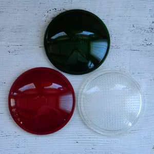May include: Three round glass lenses, one green, one red, and one clear. The lenses are on a white wooden surface.