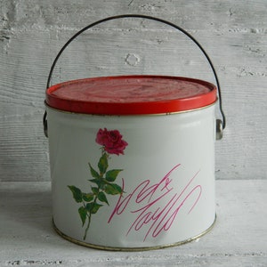 May include: White metal tin with a red lid and a black handle. The tin has a pink rose and the words "Made with Love" written in pink.
