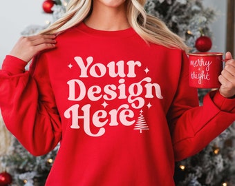 May include: Red sweatshirt with the text "Your Design Here" in pink lettering with a small Christmas tree graphic. The sweatshirt is being modeled by a person holding a red mug with the text "merry + bright" in white lettering.