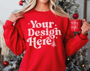 May include: Red sweatshirt with the text "Your Design Here" in pink with a small Christmas tree graphic. The sweatshirt is being modeled by a person holding a red mug with the text "merry + bright" in white.