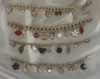 May include: Four gold charm bracelets with various charms, including a crown, a butterfly, a star, a flower, a key, a heart, an eye, a moon, a turtle, a crown, a star, a flower, a bow, a smiley face, a letter B, a leaf, a pearl, a red lip, a bell, a strawberry, a black flower, a starfish, a crown, a flower, and a bow.