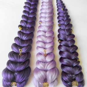 May include: Three long, thick synthetic hair braids arranged vertically. The outer braids are a deep violet purple, while the center braid is a light lavender. Each braid features metallic gold hair cuffs and small star-shaped charms.