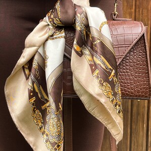May include: A brown and beige patterned silk scarf tied around a brown leather handbag with a crocodile embossed design.