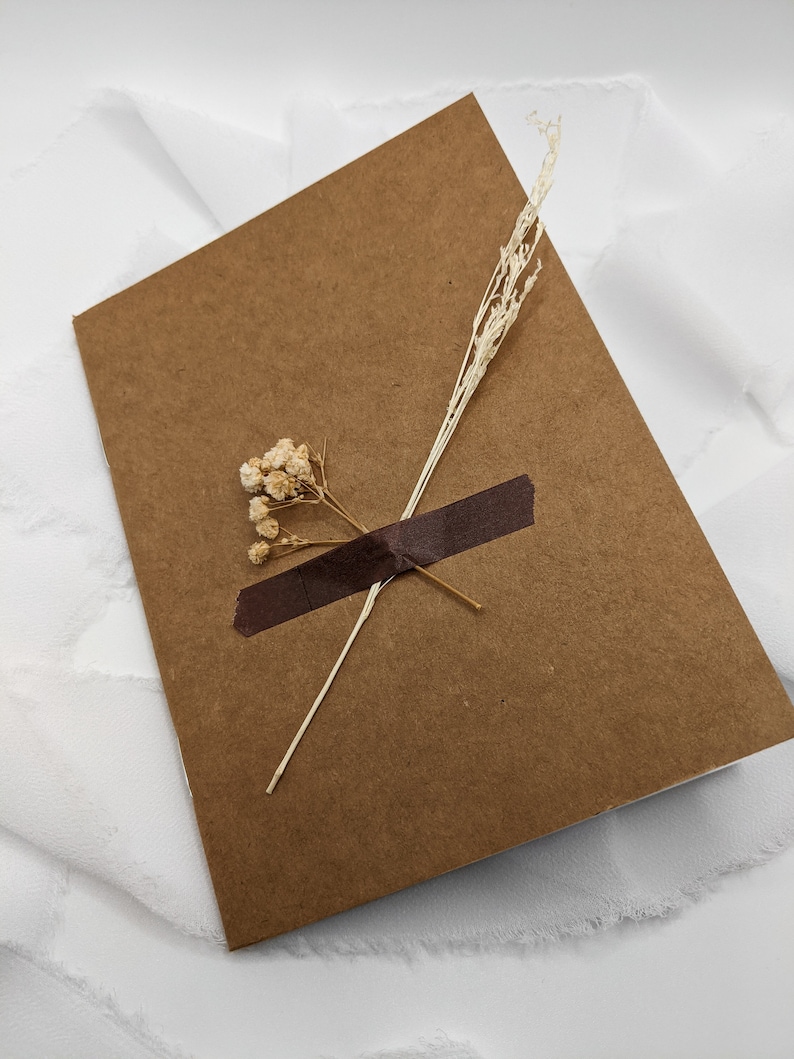 May include: A brown card with a piece of brown tape and dried flowers on top. The card is on a white background.