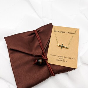 May include: A brown velvet pouch with a gold chain necklace featuring a small cross pendant. The card attached to the necklace reads "Proverbs 31 Woman" and "A woman who fears the Lord is to be praised. Proverbs 31:30".