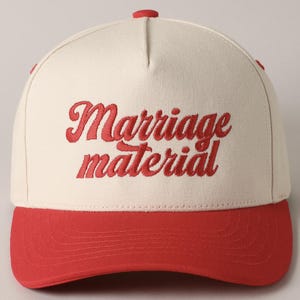 May include: A white and red baseball cap with the text "Marriage material" embroidered in red on the front.