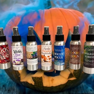 May include: Seven silver metal spray bottles with black caps, each featuring a unique label: Trick or Treat, Witches Brew, Poison Pie, Vanilla Pumpkin Marshmallow, Hocus Pocus, Candy Corn, and Twilight Forest, arranged in a row.