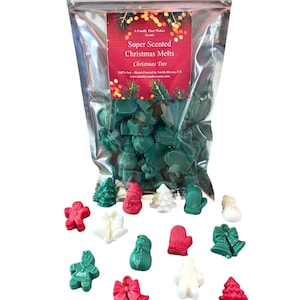 Pode incluir: Um saco de derretimentos de cera verde, vermelho e branco em forma de &aacute;rvores de Natal, enfeites, bonecos de neve e luvas. O saco tem um r&oacute;tulo que diz "Super Scented Christmas Melts Christmas Tree".