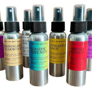 May include: A collection of aluminum spray bottles with black caps and colorful labels. Scents include Black Amber Lavender, Mahogany Teakwood, Seaside Serenity, Pineapple Sage, and Fresh Roses. Each bottle is labeled with the scent name and the words "Room Spray / Poo-Pourri".