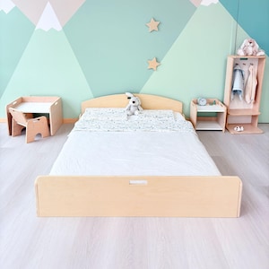 May include: A light wood-toned bedroom set with a bed, nightstand, and wardrobe. The bed has a white comforter and a patterned pillowcase. A small table and chair set are on the left. The wall is painted with a mountain scene.