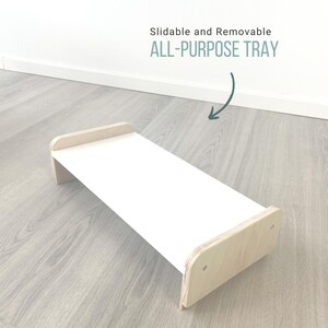 May include: A white, rectangular tray with wooden edges. The tray is slidable and removable. The text "ALL-PURPOSE TRAY" is written in green on a white background.