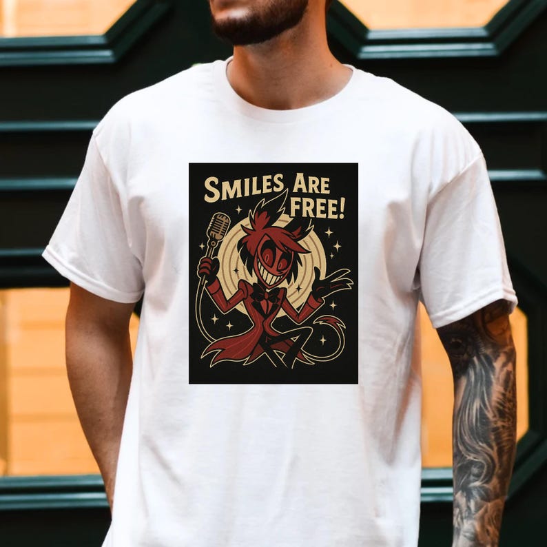 May include: White t-shirt featuring a graphic of a cartoon character holding a microphone, with the text "SMILES ARE FREE!". The character is in a red suit with a black background and a yellow circle.