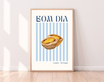 May include: A framed print showing two pastel de nata pastries against a blue and white striped backdrop. The words "BOM DIA" are at the top, with "Lisbon, Portugal" at the bottom. The frame is made of light-colored wood.