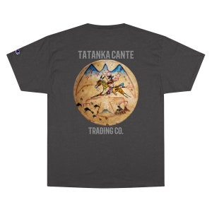 May include: Dark gray Champion t-shirt featuring a circular graphic with a Native American theme. The graphic depicts a person on horseback, with the text "TATANKA CANTE" above and "TRADING CO." below. The Champion logo is visible on the sleeve.