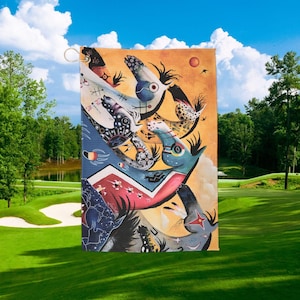 May include: A rectangular garden flag featuring an abstract design with various shapes and colors, including blue, red, and orange. The artwork has a whimsical style with a gold-colored hanging loop at the top. The flag is displayed outdoors against a backdrop of a golf course and blue sky.