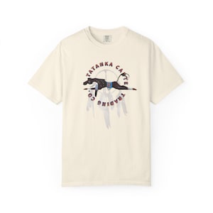 Könnte beinhalten: Cremefarbenes T-Shirt mit einer Grafik eines schwarzen Pferdes mit indianischem Design, umgeben von den Worten "TATANKA CAFE TRADING CO." in einem kreisförmigen Muster. Unter dem Pferd befinden sich stilisierte Federn.