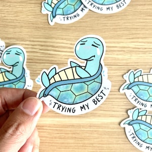 May include: A sticker featuring a cartoon turtle with a blue and green shell, wearing a blue life preserver. The turtle has a sad expression and is crying. The sticker has the text "Trying my best" written on it.