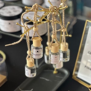 Könnte beinhalten: Ein goldfarbener Metallständer mit runder Oberseite und drei Beinen hält mehrere kleine Glasflaschen mit Etiketten. Die Etiketten haben unterschiedliche Texte, darunter "daydream", "so this is love" und "caramel vanilla".