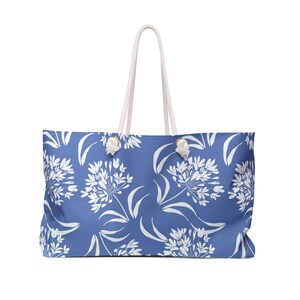May include: A blue tote bag with white floral print. The bag has white rope handles.