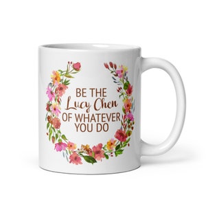 May include: White ceramic mug with a floral wreath design. The text "Be the Lucy Chen of whatever you do" is printed in brown on the mug.