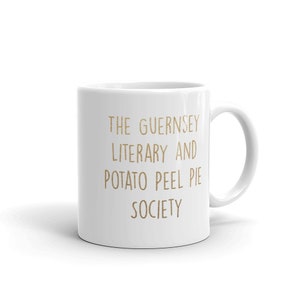 May include: White ceramic mug with a gold inscription that reads "The Guernsey Literary and Potato Peel Pie Society."
