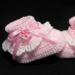May include: A pair of pink crocheted baby booties with white lace trim and pink satin bows.