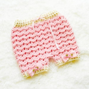 May include: Pink crocheted baby shorts with a white crocheted trim and pink satin bows.