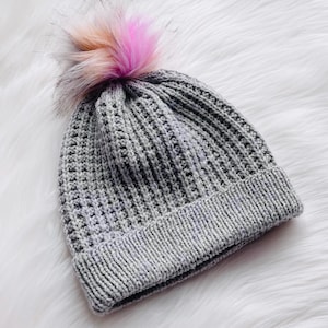May include: A gray knitted beanie with a fluffy pink and white pom pom on top.