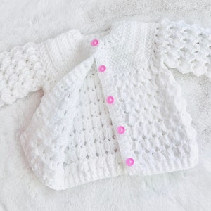 May include: White crocheted baby cardigan with pink buttons.