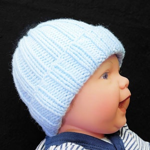 May include: A baby wearing a light blue knitted hat and a striped shirt. The hat has a ribbed texture.