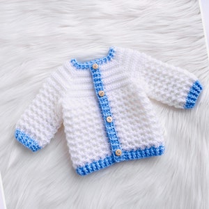 May include: White crocheted baby cardigan with blue trim and wooden buttons.