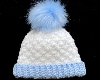 Könnte beinhalten: Weiße Häkelmütze für Babys mit blauem Bommel und blauem Häkelrand.
