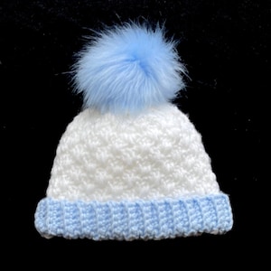 May include: White crocheted baby hat with a blue pom pom and a blue crocheted brim.