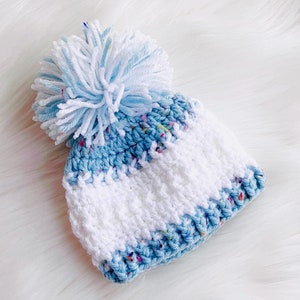 May include: A blue and white striped knitted hat with a white pom-pom on top. The hat has a speckled blue stripe.