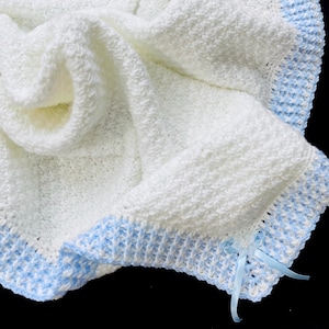 May include: White crocheted baby blanket with a blue and white crocheted border and a blue satin ribbon.
