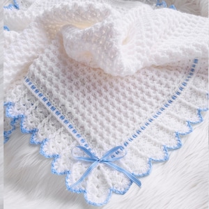May include: White crocheted baby blanket with a blue satin ribbon tied in a bow. The blanket has a scalloped edge and a blue trim.
