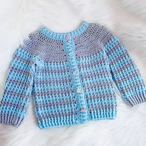 May include: A blue and gray striped crocheted cardigan with colorful buttons. The cardigan has a button-up front and long sleeves.