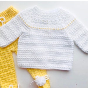 May include: A white crocheted sweater with a yellow trim around the neckline and a pair of yellow crocheted trousers with white pom-poms on the feet.