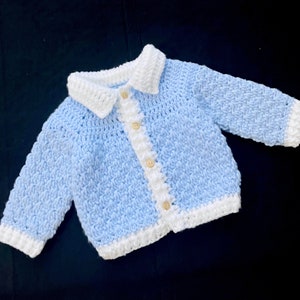 May include: A light blue crocheted baby cardigan with a white collar and button closure.