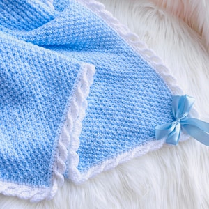 May include: A light blue crocheted baby blanket with a white crocheted border and a light blue satin bow.