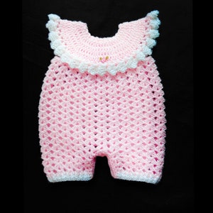 May include: A pink crocheted baby onesie with white trim and a white crocheted collar. The onesie has a small pink flower embellishment on the collar.